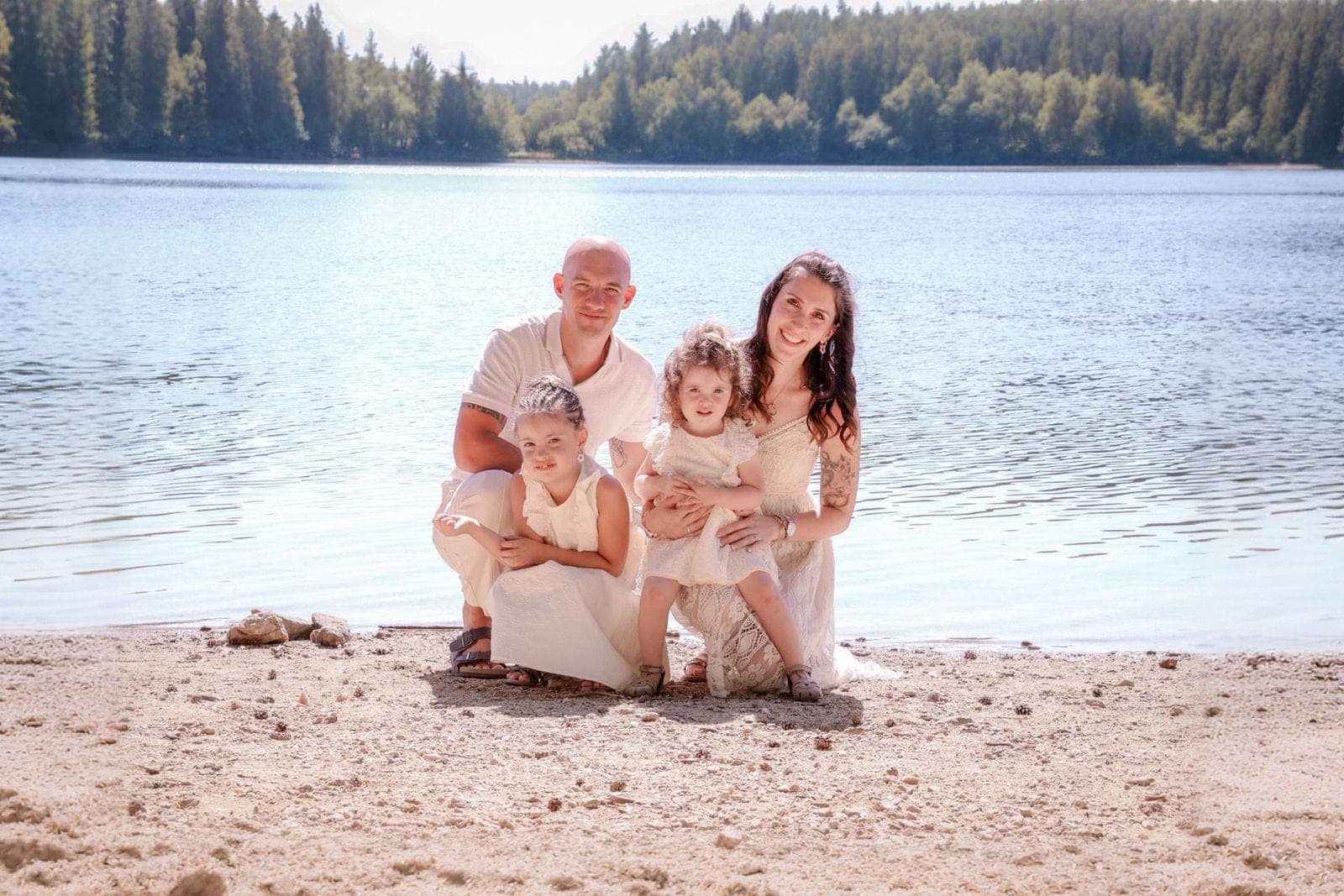 Une famille en tenues claires, assise sur une plage au bord d’un lac.