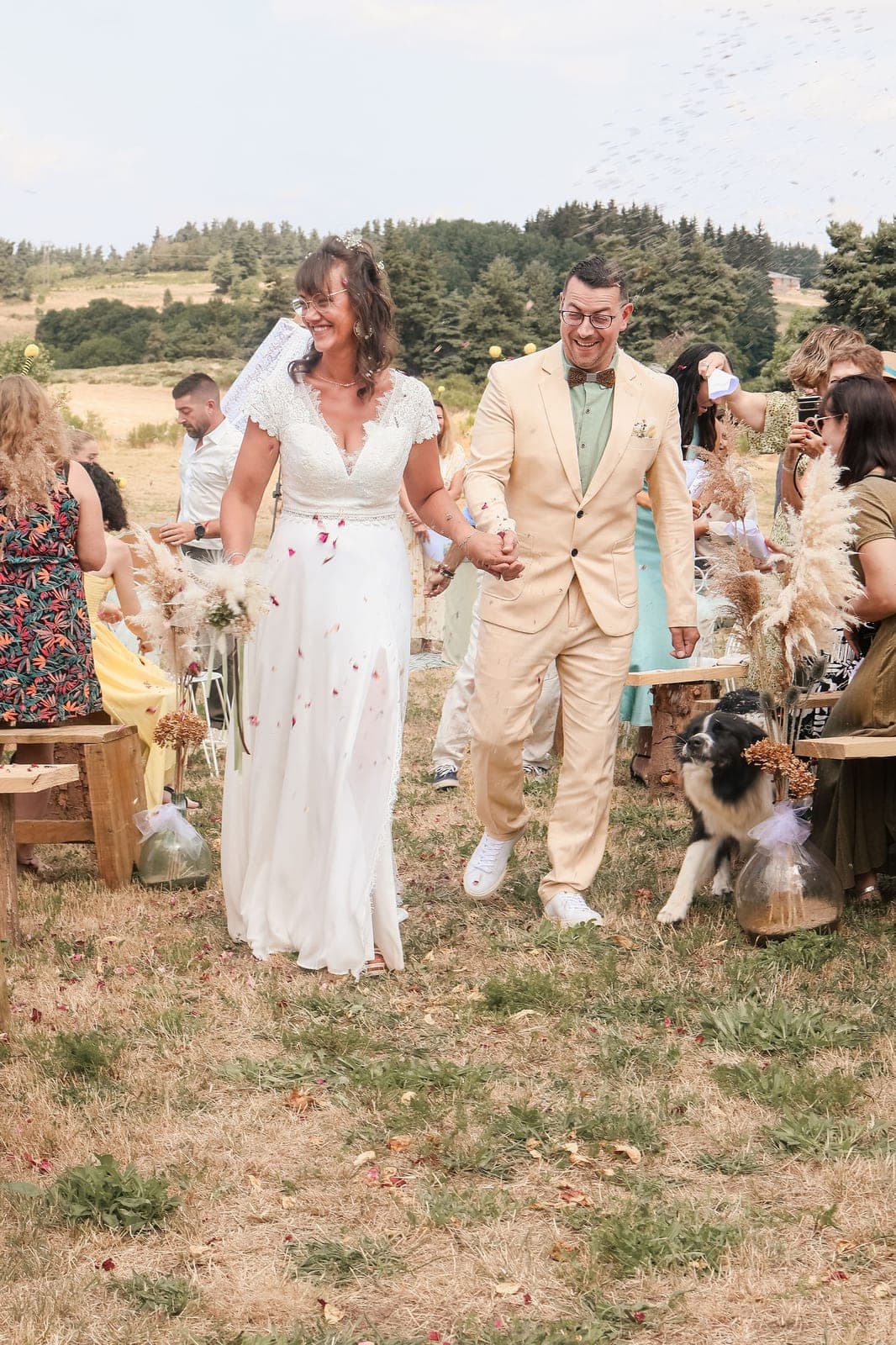 Des mariés remontent l’allée sous les confettis, leur chien à leurs côtés.