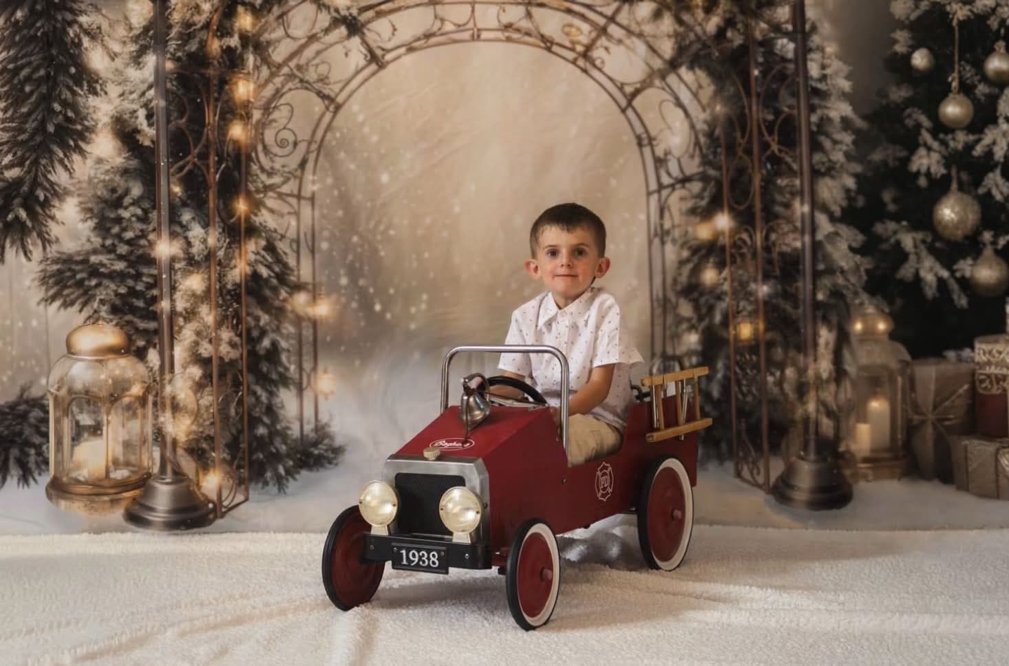 Petit garçon au volant d’une voiture à pédales rouge, dans un décor de Noël enneigé sous une arche lumineuse