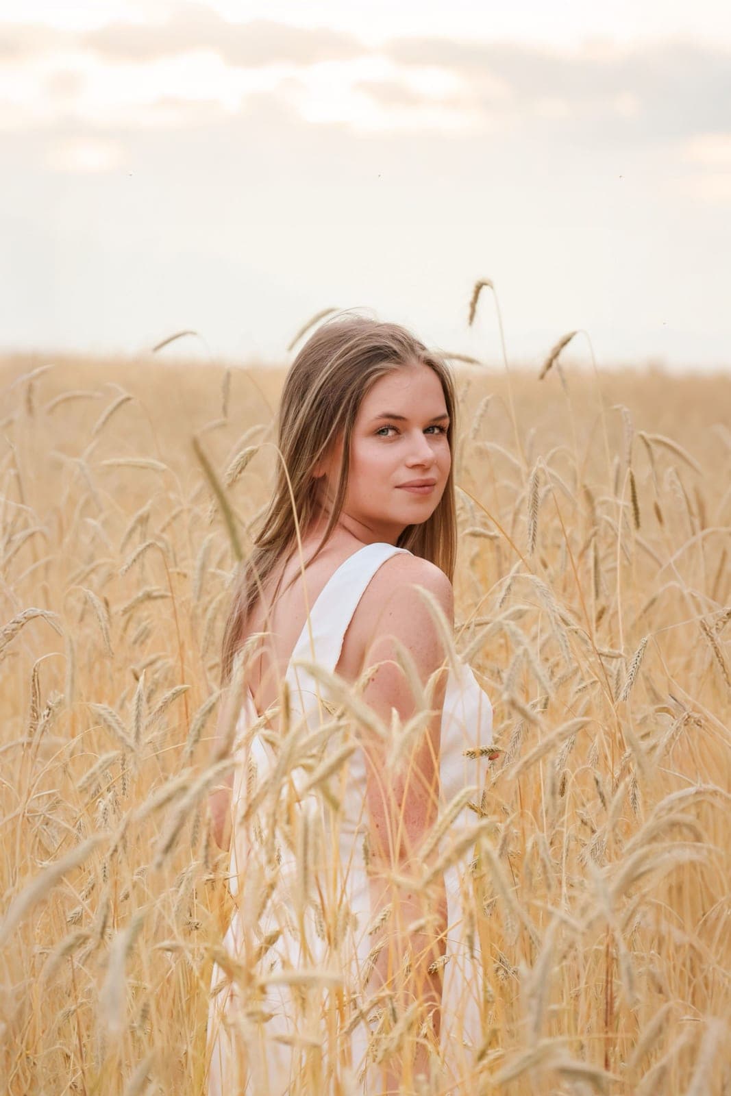 Portrait d’une jeune femme au milieu d’un champ de blé, à la lumière du soir.